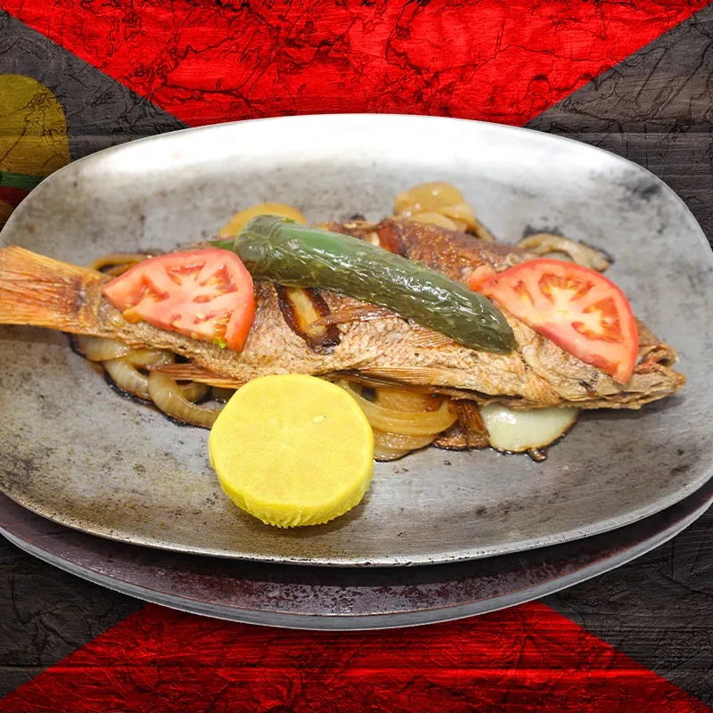 Whole golden fried fish, garnished with tomato, chili, onions, lemon.