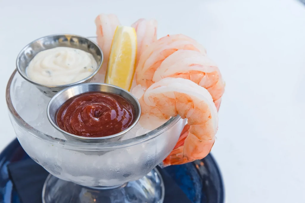 Shrimp cocktail on crushed ice with lemon and two dipping sauces.