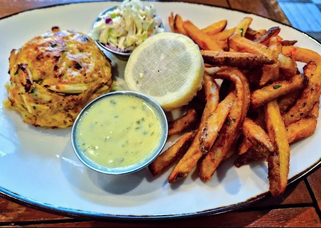 Golden-brown crab cake, crispy fries, sauce, coleslaw, and lemon.
