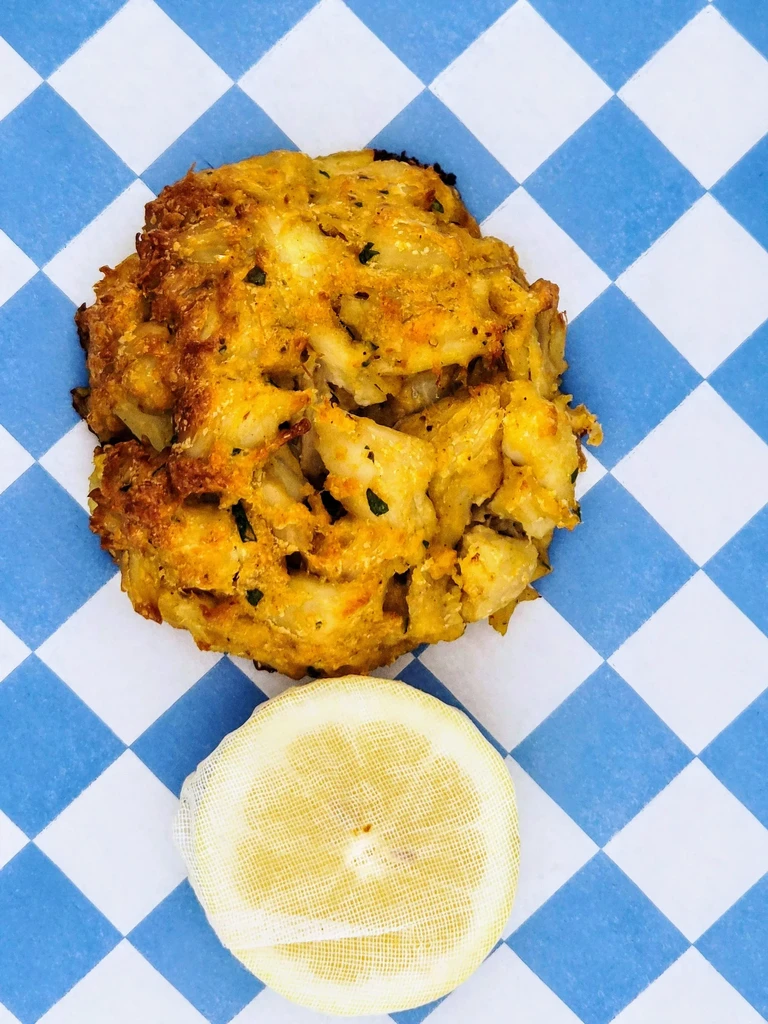 Golden-brown crab cake and mesh-wrapped lemon on checkered paper.