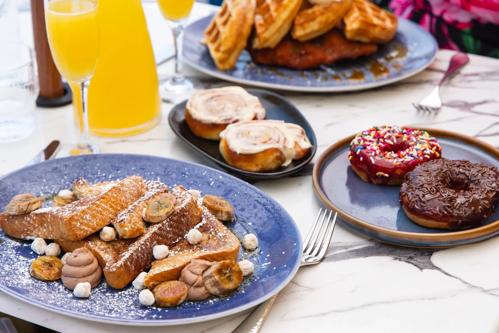 Restaurant brunch with French toast, donuts, cinnamon rolls, waffles, mimosas.