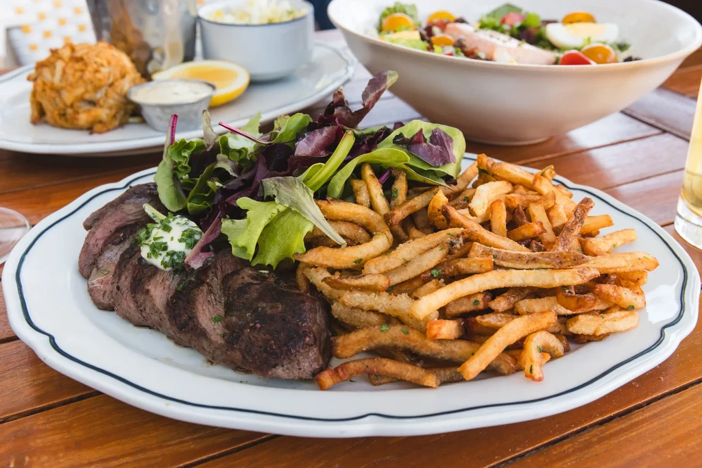 Grilled steak, french fries, and green salad on a restaurant table.
