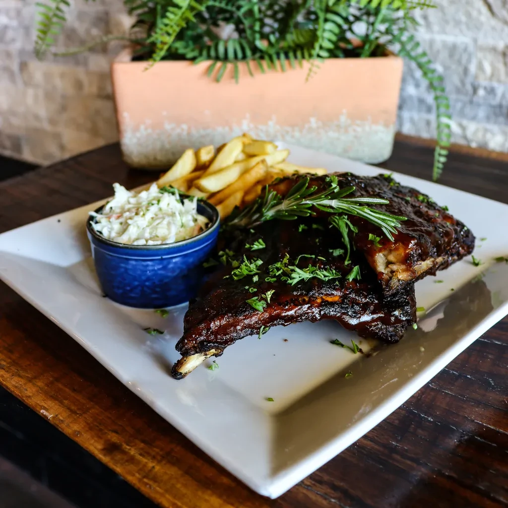 BBQ ribs with coleslaw and french fries on a white plate.