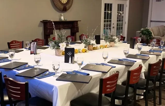 Elaborately set U-shaped table with seasonal decor in an empty dining room.