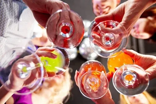 Multiple hands clinking colorful drinks in stemware during a toast.