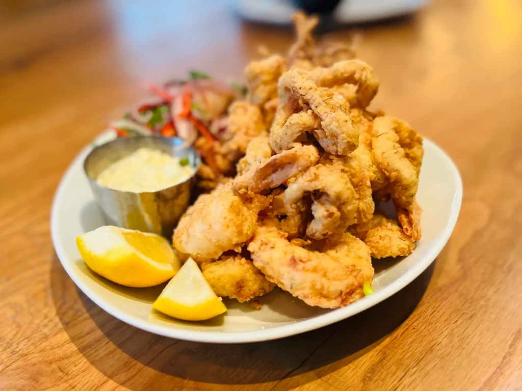 Close-up of golden-brown fried seafood, dipping sauce, lemon, and salad.