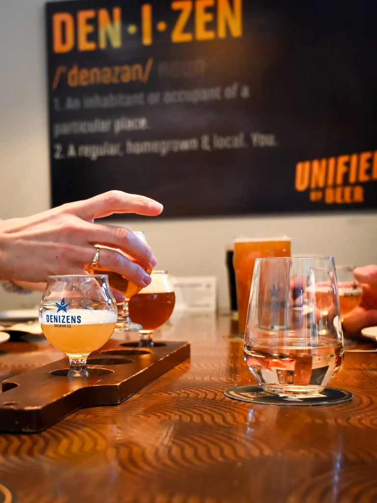 Person's hand reaches for a Denizens beer flight at a brewery.