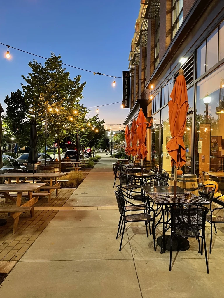 Empty outdoor patio at dusk with orange umbrellas and string lights.