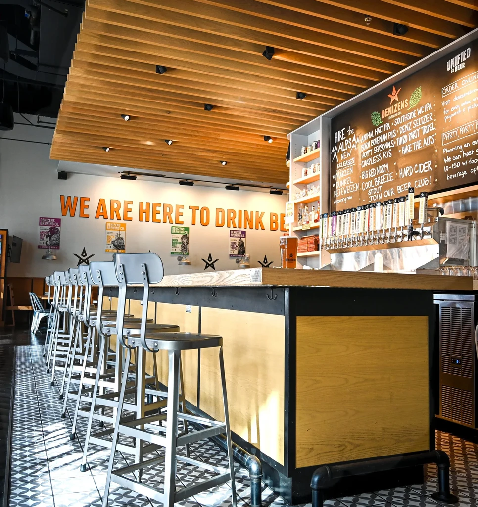Denizens Brewing Co. bar counter with taps, menu, and stools.