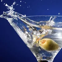 Splashing martini glass with a green olive on a blue background.