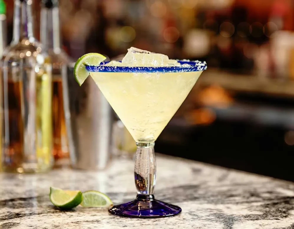 Pale green margarita in a blue-rimmed martini glass with lime.