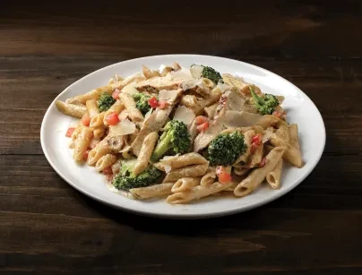 Creamy chicken, broccoli, tomato pasta with Parmesan, on a wooden surface.