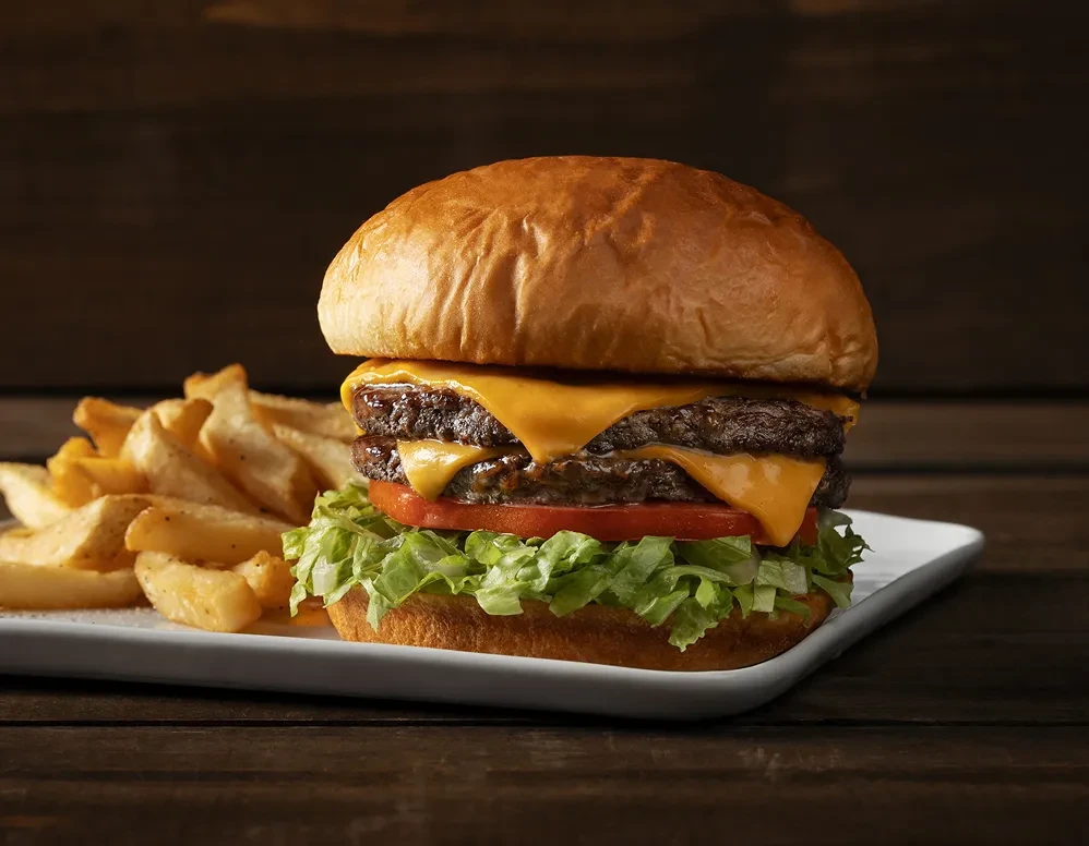 Double cheeseburger with melted yellow cheese, lettuce, tomato, and wedge fries.