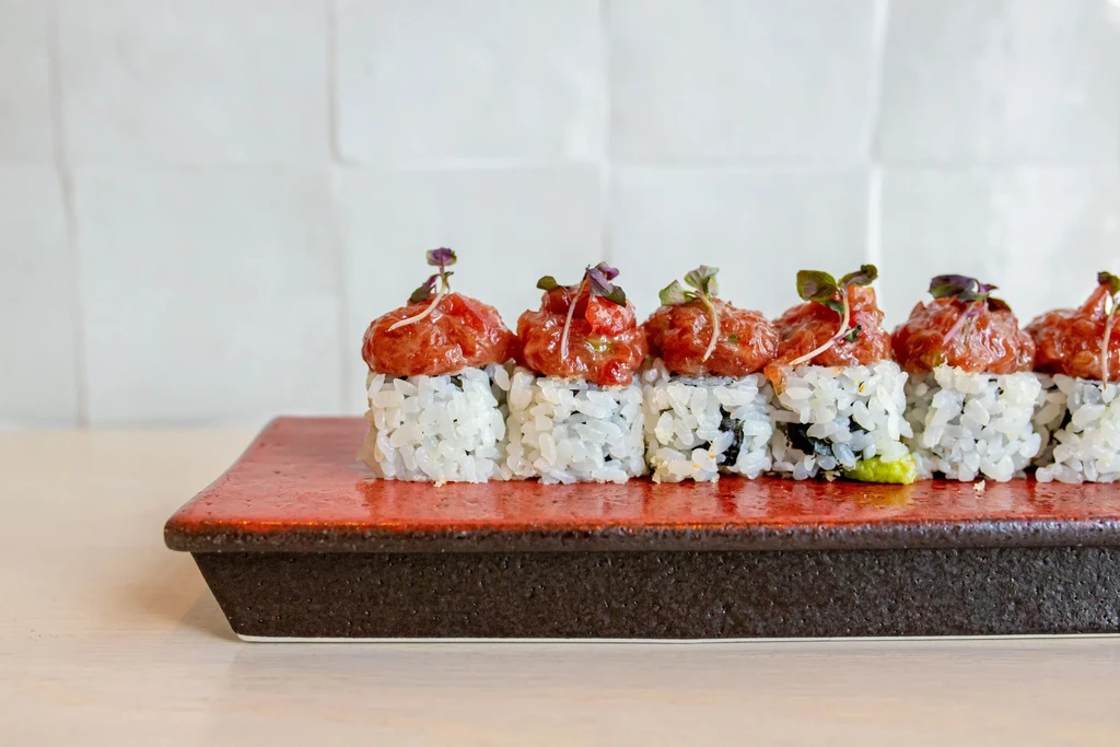 Seven uramaki sushi rolls topped with spicy tuna and microgreens.