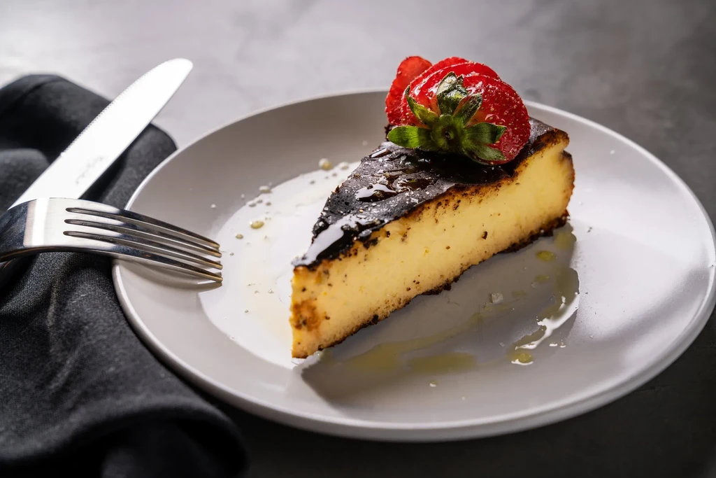 Slice of Basque burnt cheesecake, dark top, strawberries, cutlery.