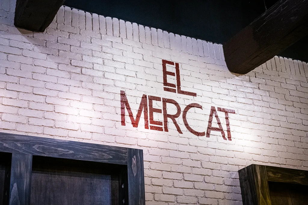 White brick wall with 'EL MERCAT' text, illuminated from below.