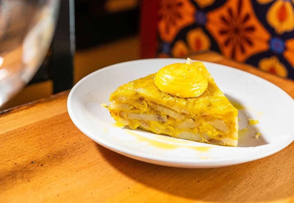 Thick slice of potato tortilla topped with yellow sauce on plate.