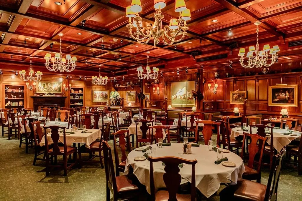 Elegant, empty restaurant with dark wood, chandeliers, and set tables.