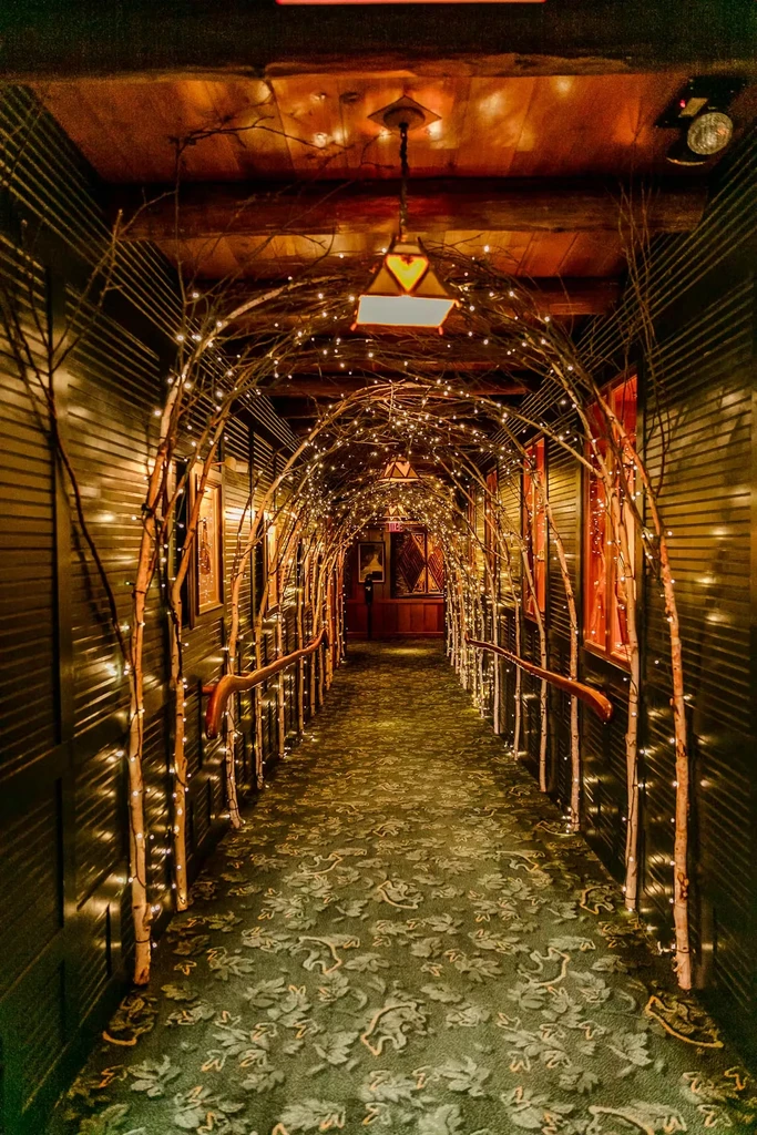 Warmly lit corridor with arching branches and twinkling string lights.