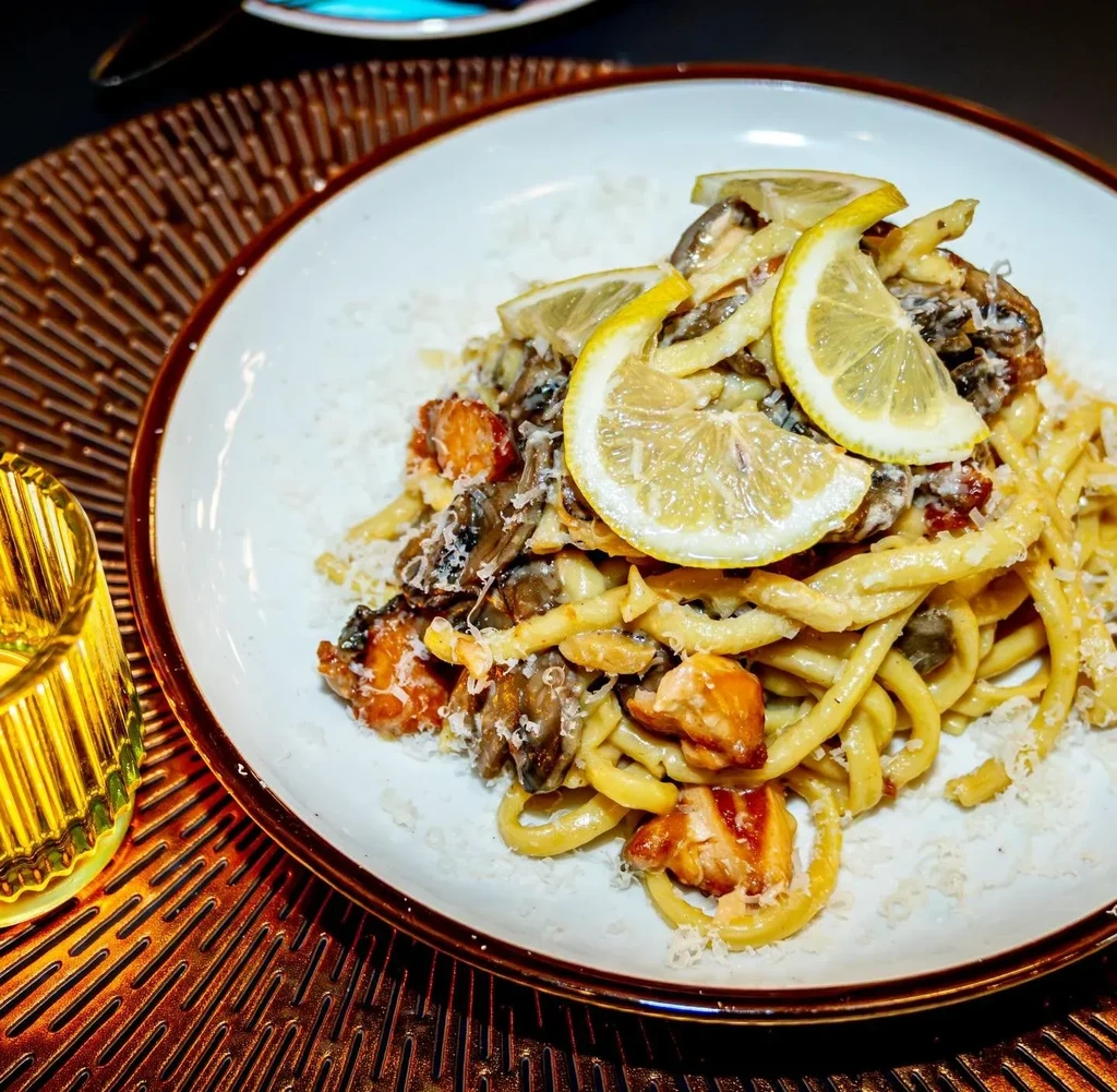 Thick pasta with salmon, mushrooms, cheese, and lemon slices.