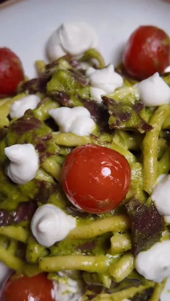 Close-up of pasta with green pesto, cherry tomatoes, and mozzarella.