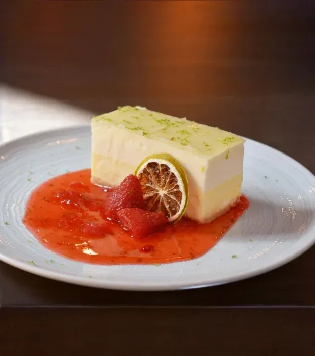Rectangular two-layered dessert with green zest, red sauce, and citrus slice.