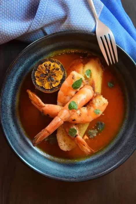 Three shrimp on toast in red sauce, with lemon and herbs.