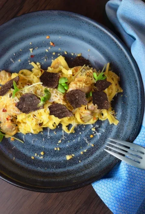 Pasta with black truffles, cheese, microgreens, and a fork.