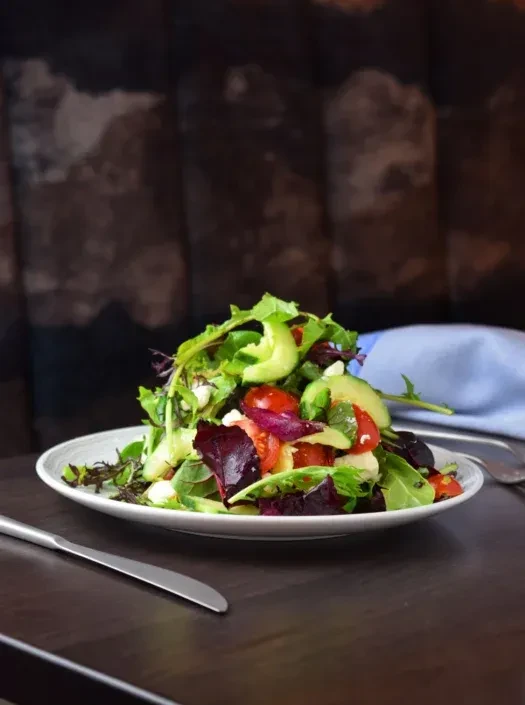 Fresh salad with greens, avocado, tomatoes, cheese, and a knife.