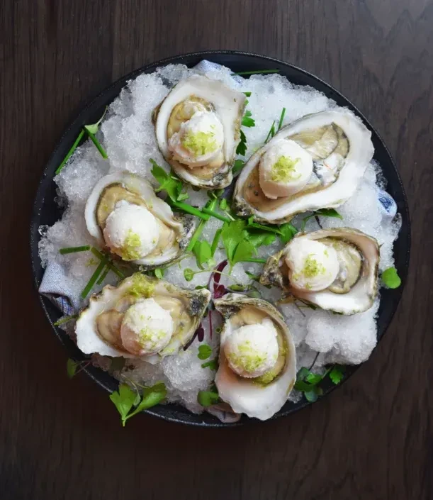 Six shucked oysters on ice, topped with cream and green zest.