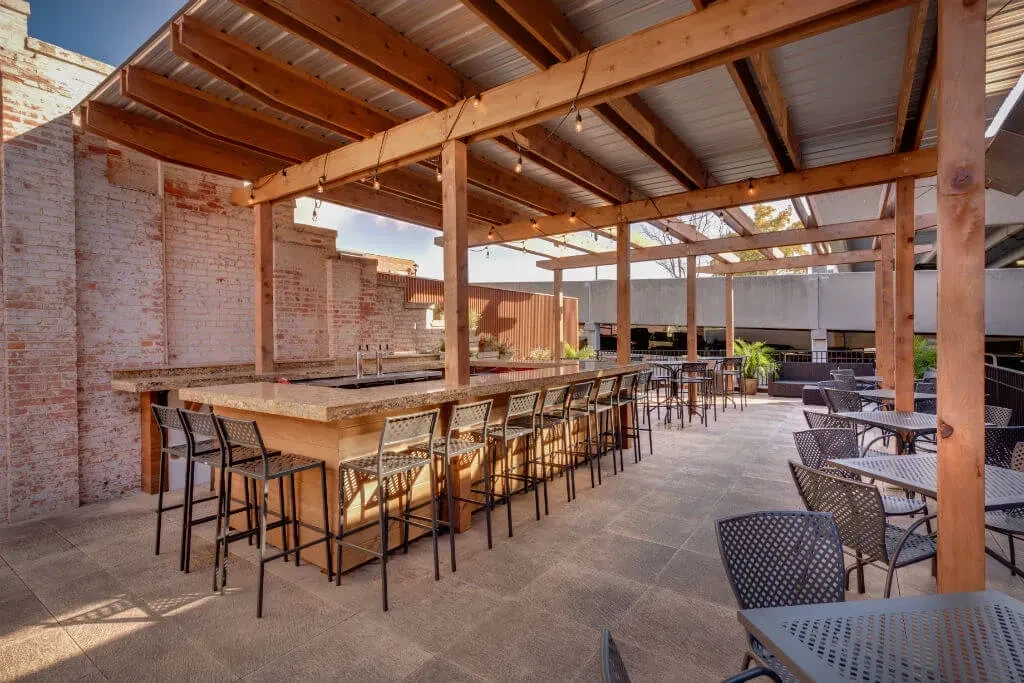 Outdoor patio bar with brick wall, black seating, and wooden pergola.