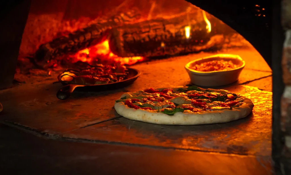 Pizza, pan, and bowl cooking in a fiery wood-fired oven.