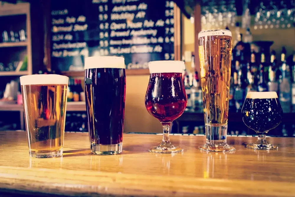 Five diverse beers in glasses lined on a wooden bar.