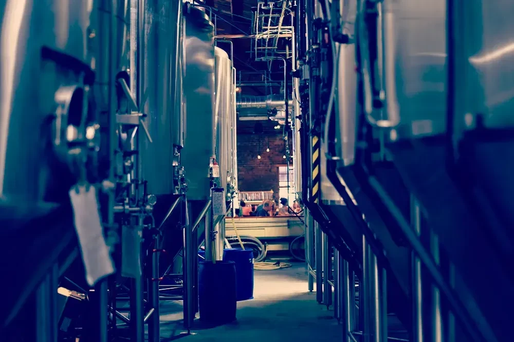 Industrial tanks line an aisle leading to a blurred bar.