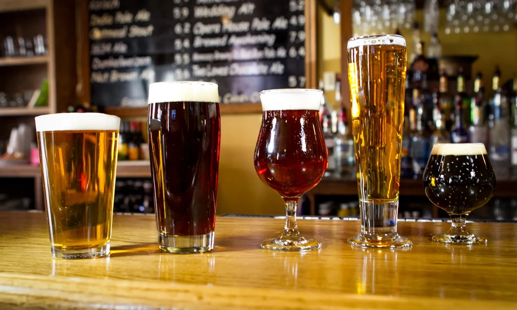 Five different beers in varied glasses on a wooden bar.