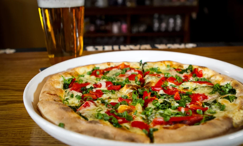 Pizza with melted cheese, red bell peppers, green onions, and a beer.
