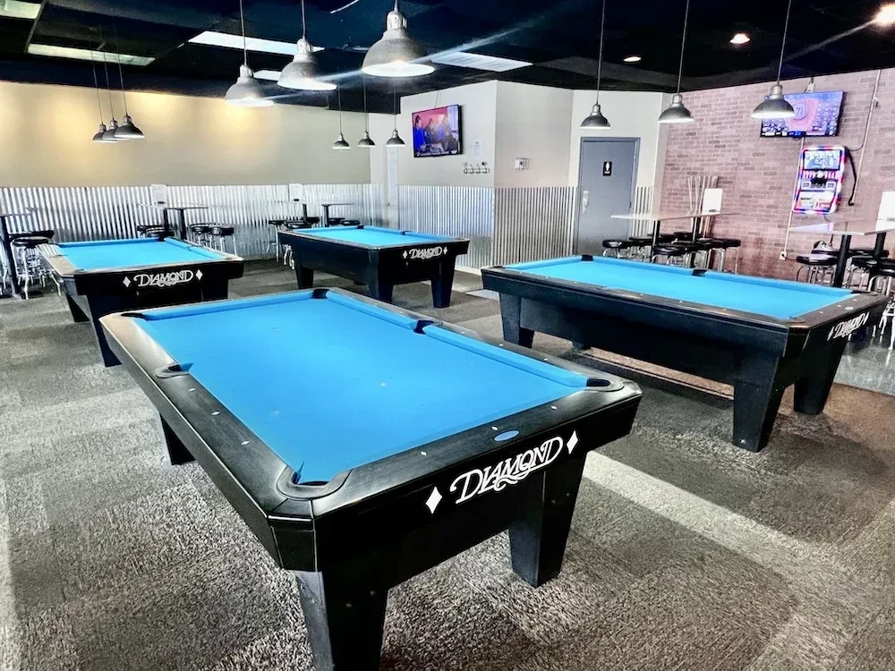 Four black pool tables with blue felt in an industrial hall.
