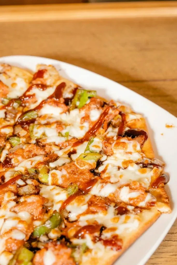 Rectangular pizza with chicken, cheese, peppers, and two sauces.