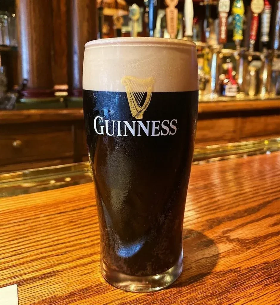 Guinness pint glass with condensation and logo on a wooden bar.