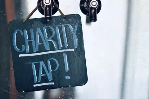 Dark chalkboard sign on tap reads 'CHARITY TAP!'.