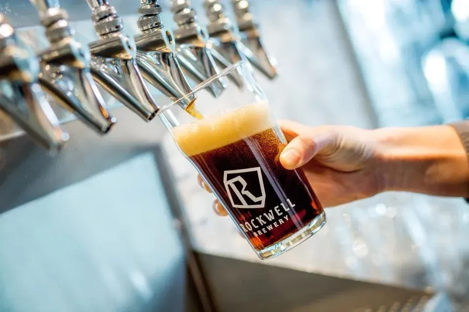 Dark beer pours into a branded Rockwell Brewery glass.
