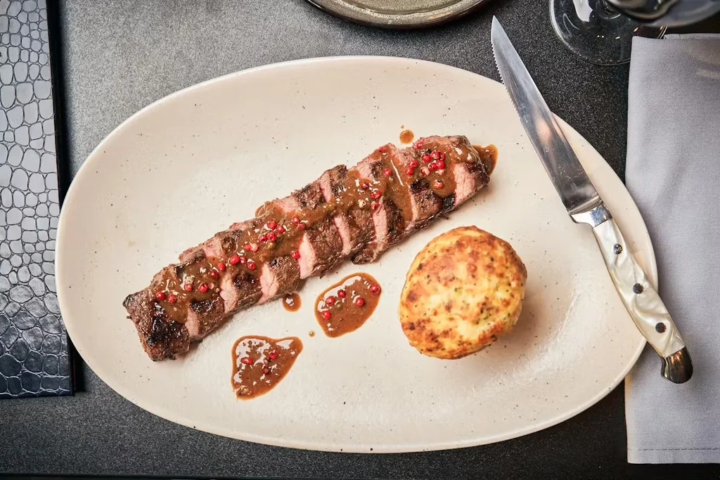 Overhead view: Plated sliced medium-rare steak, brown sauce, pink peppercorns, side.