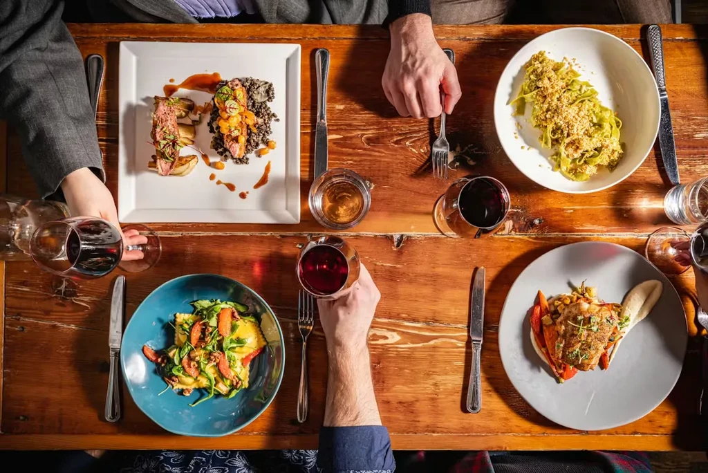 Top-down view of multiple dishes and hands dining at a wooden table.