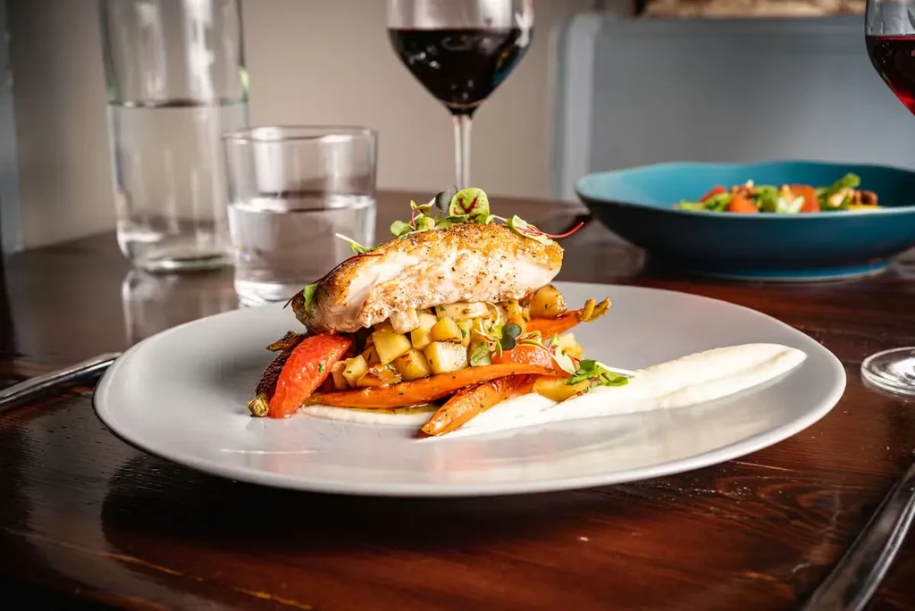 Pan-seared white fish on vegetables, garnished with sauce and microgreens.