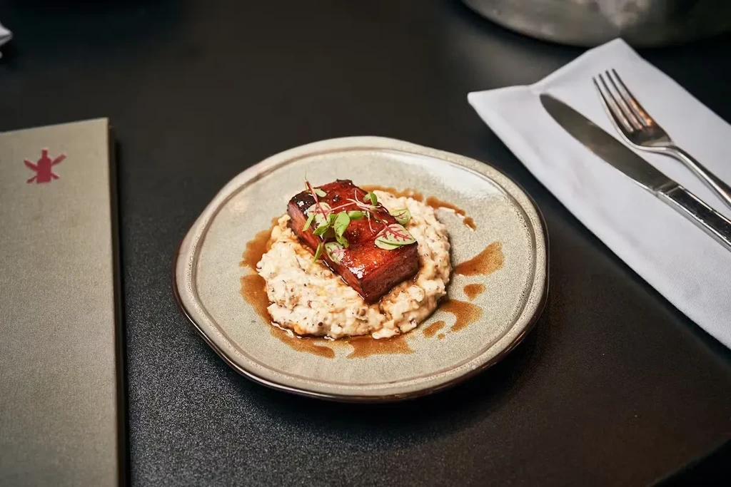 Glazed meat, microgreens, creamy bed, and sauce on a rustic plate.