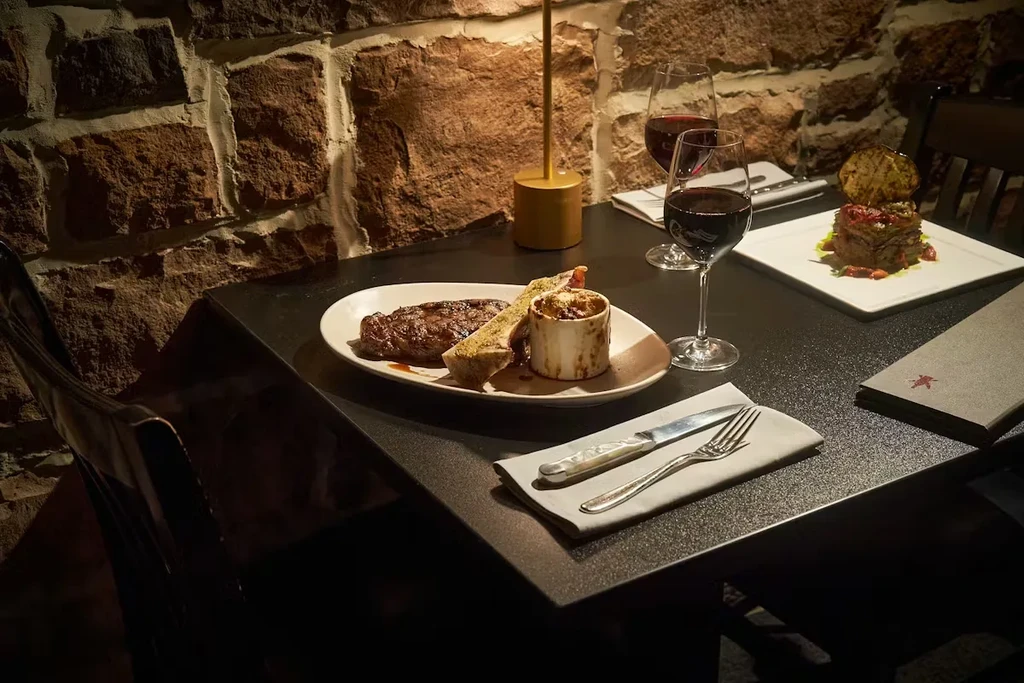 Two gourmet dishes and red wine on a dimly lit restaurant table.