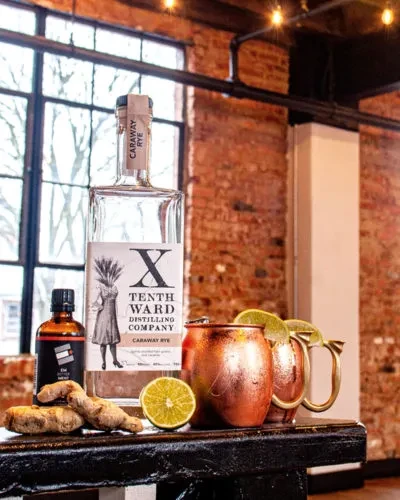 Tenth Ward Caraway Rye, copper mugs, ginger, lime in industrial setting.