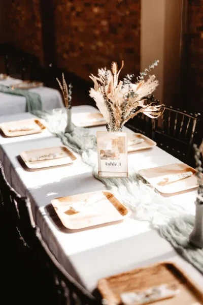 Event table with sage runner, natural plates, dried flowers against brick wall.