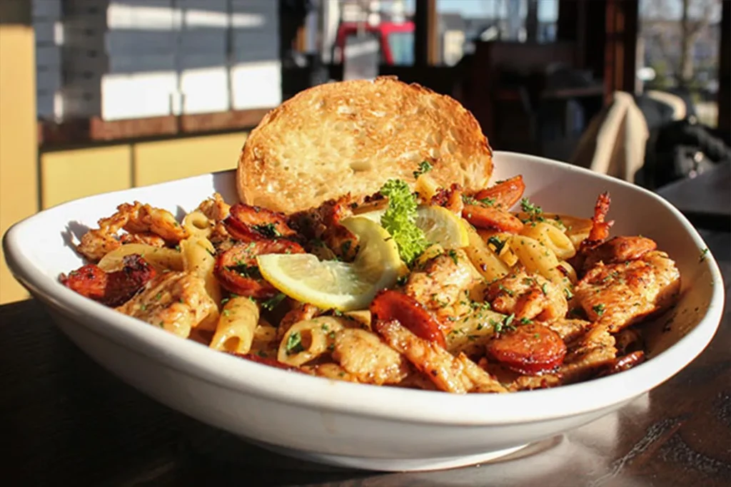 White bowl of pasta with chicken, sausage, lemon, and crusty bread.