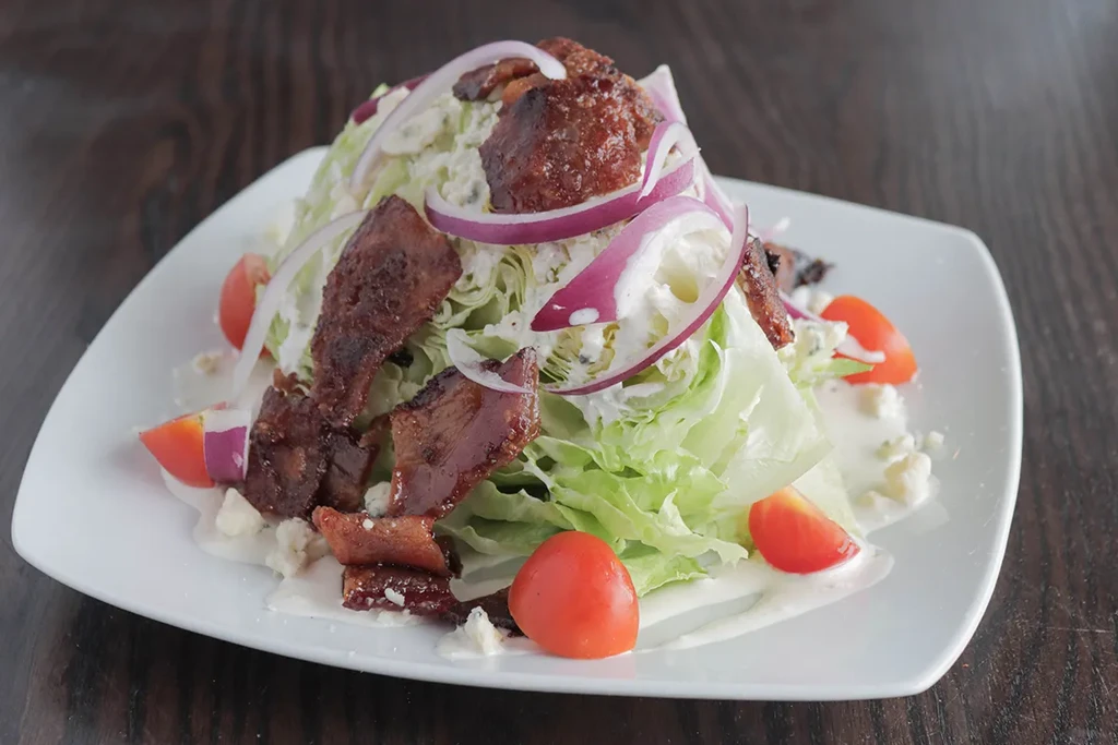 Wedge salad with iceberg lettuce, bacon, tomatoes, red onion, blue cheese.